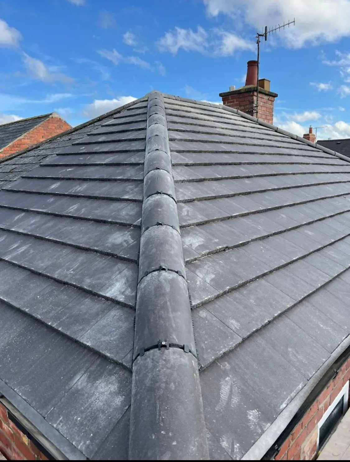Quality installation of a grey tiled pitched roof with dry-fixed ridge tiles.