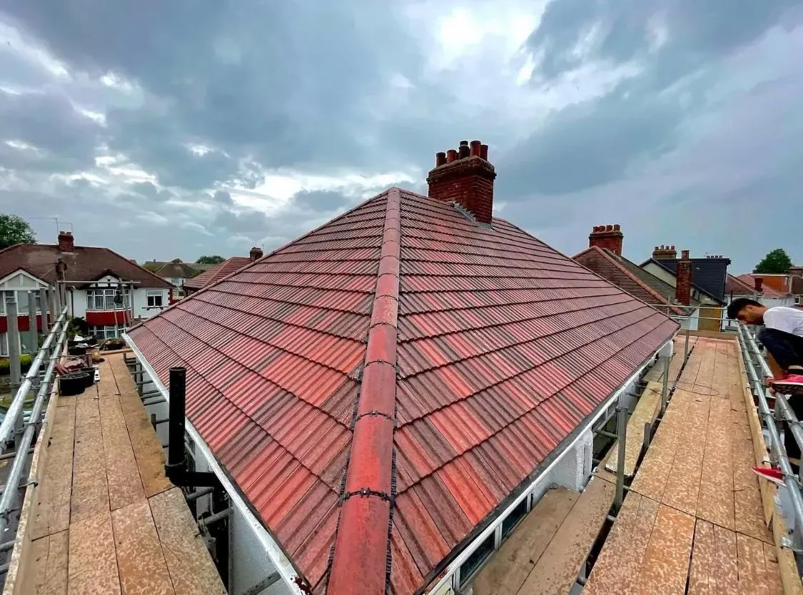 Newly installed or repaired red tiled pitched roof on a residential home in Devon or Cornwall, with scaffolding and a roofer on site.