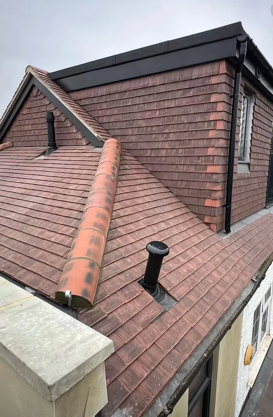 New tiled pitched roof with black flat roof section and roof vents, demonstrating quality installation.